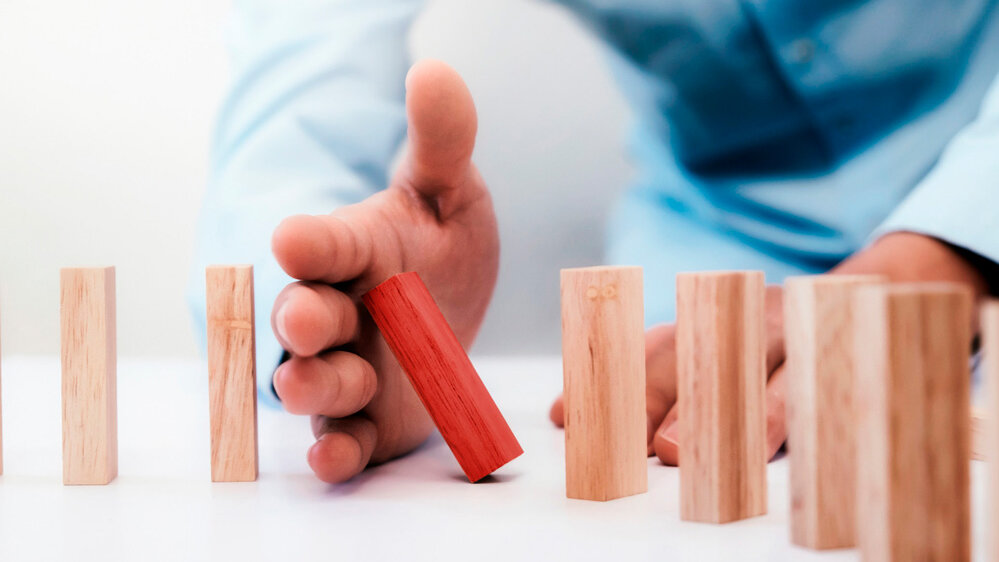 Ein roter Holzblock wird von einer Hand angehoben, während mehrere neutrale Holzblöcke in einer Reihe stehen.