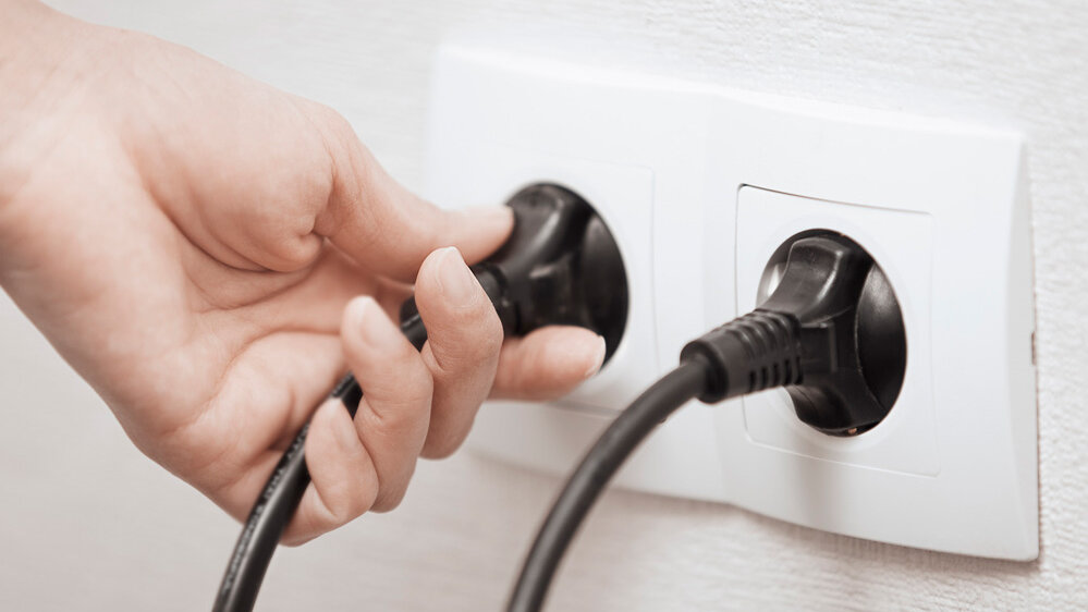 Eine Person steckt einen schwarzen Stecker in eine weiße Steckdose.