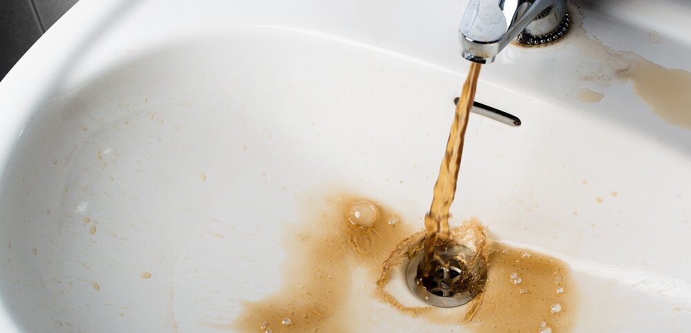 Braunes Wasser strömt aus einem Wasserhahn in ein Waschbecken.