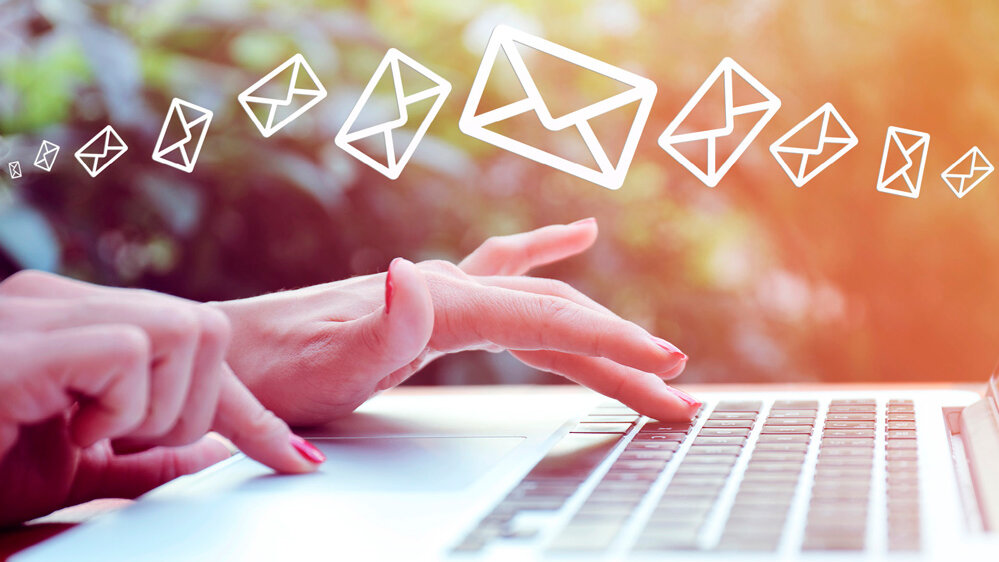 Eine Nahaufnahme einer Hand, die auf einer Laptop-Tastatur tippt, während E-Mail-Symbole in der Luft erscheinen und eine dynamische Stimmung erzeugen.